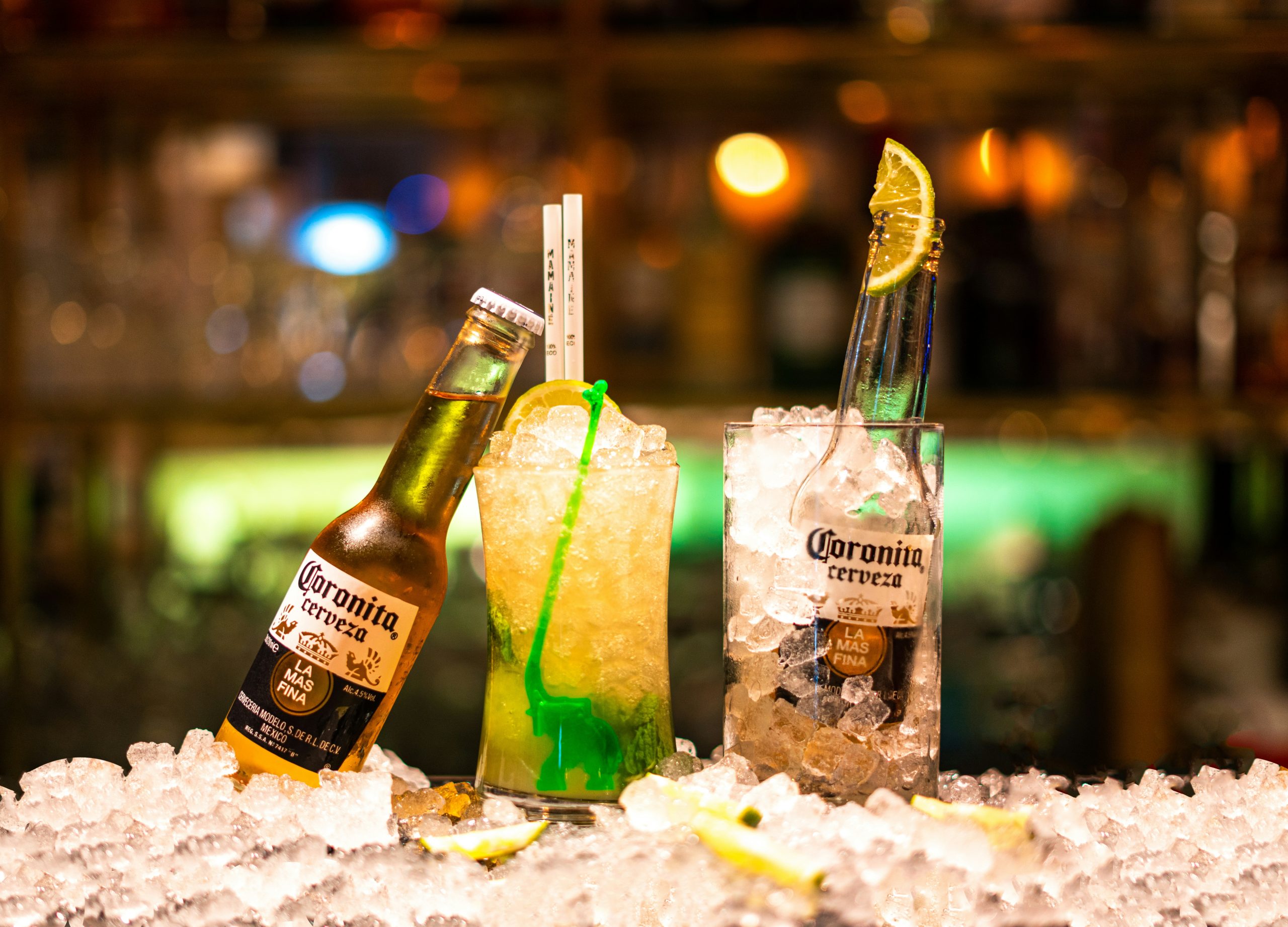 A beer mojito made with lime and rum, on a plie of ice next to bottles of Corona.