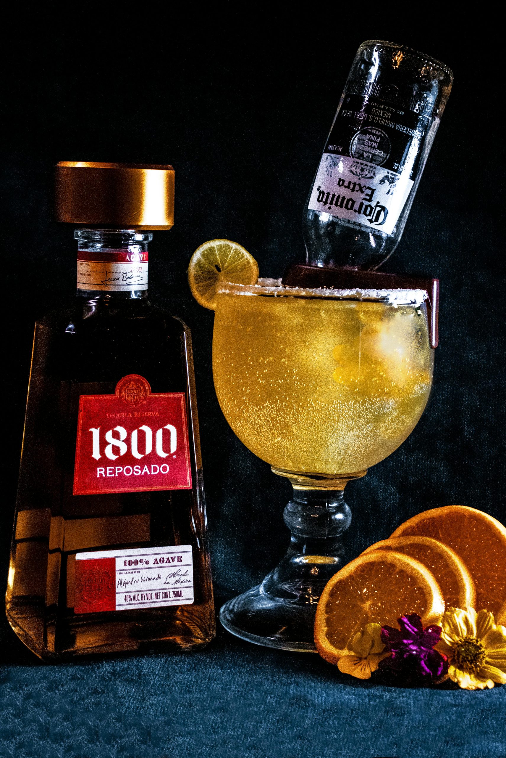 A Beergarita beer cocktail made with tequila and lime juice, next to a bottle of tequila and fruit.