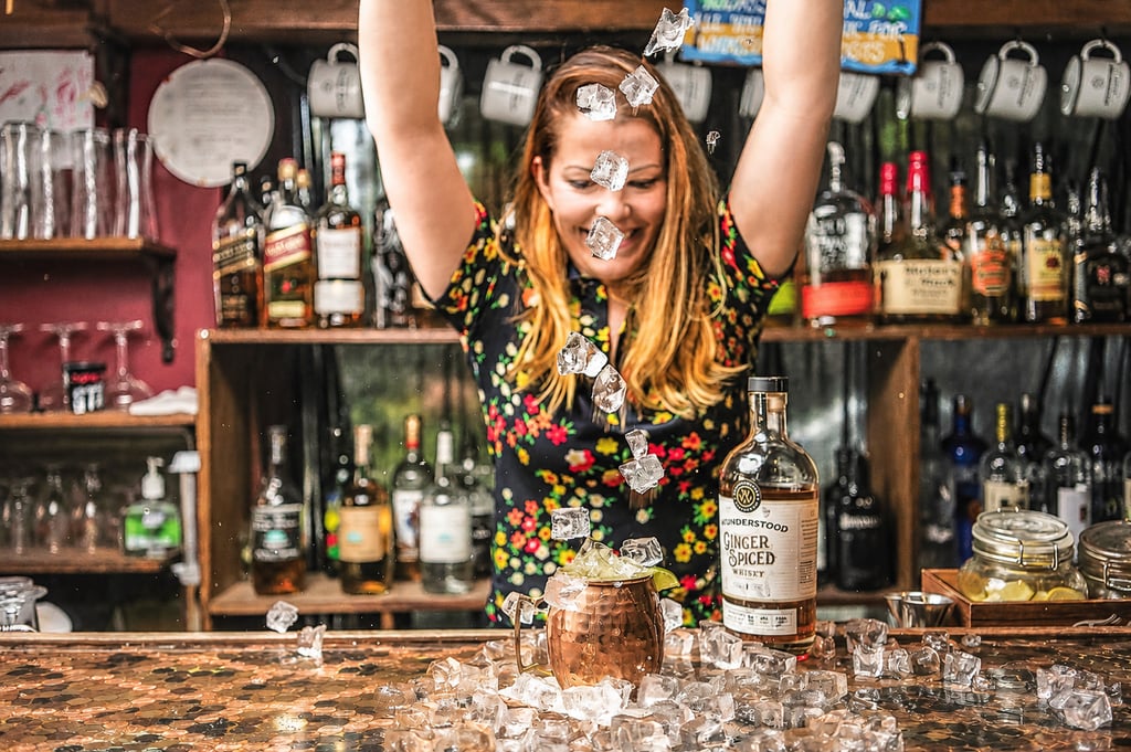 Woman pouring ice over a boubon and ginger beer drink at a bar