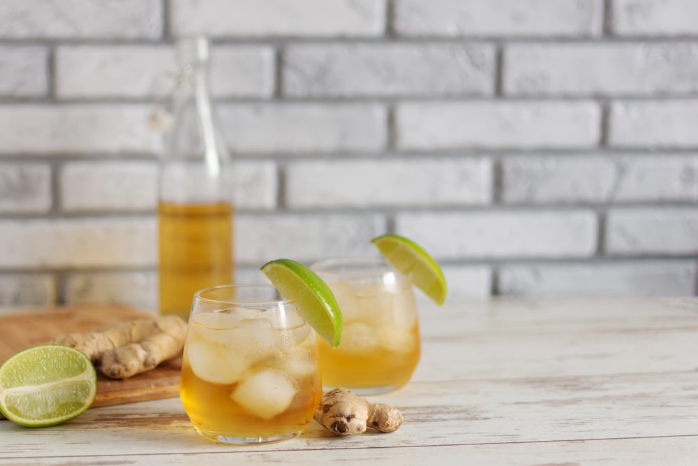 Refreshing Cold Ginger Beer with Ice and Lime served in two glasses and a bottle