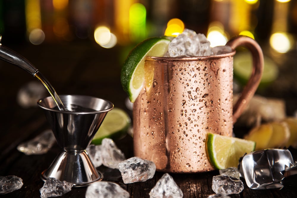 Copper vodka Mule cocktail mug filled with ice and garnished with fresh lime wedges, surrounded by ice cubes and bar tools.