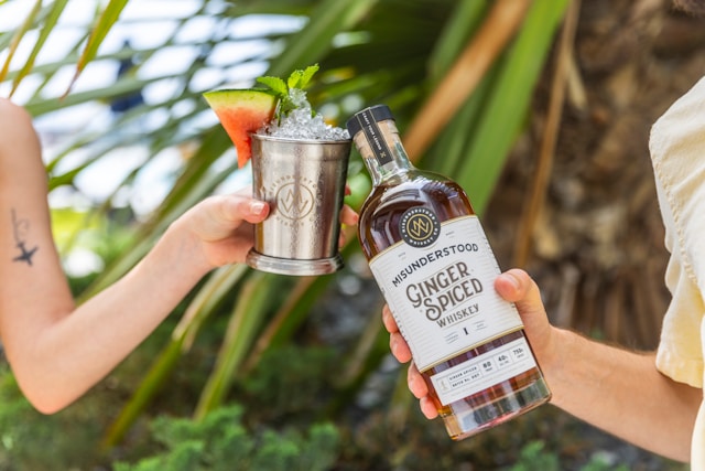 A bottle of whiskey and a kentucky mule in a tin cup being toasted next to a palm tree