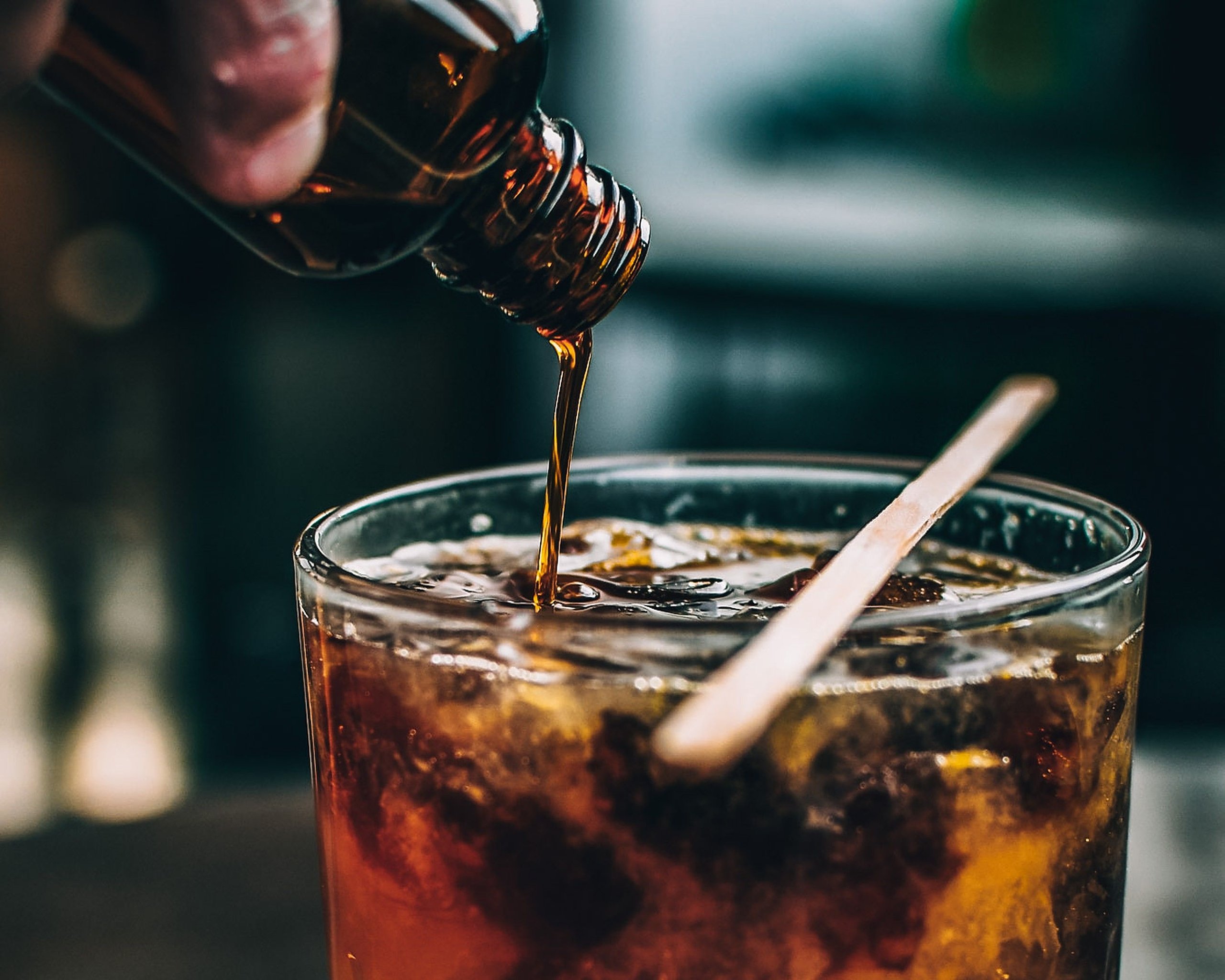 Maple syrup being poured into a bourbon cocktail