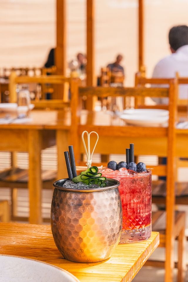 two colorful cocktails on a sunny restaurant table in Arica, Chile, with a lively atmosphere.
